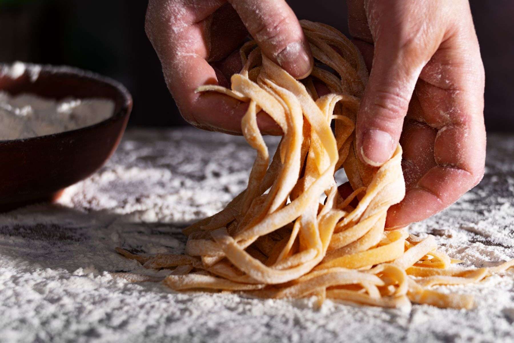 Mãos levantando fettuccine fresco recém cortado